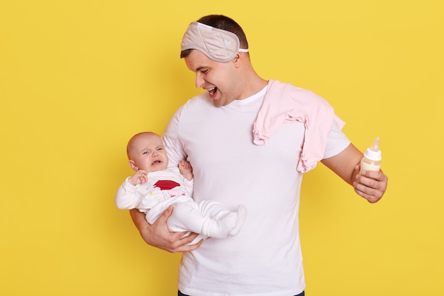 Padre con su bebé recién nacido llorando posando aislado sobre pared amarilla