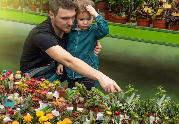 Padre y su bebé en una tienda de plantas mirando cactus. Jardinería en invernadero. Jardín botánico, cultivo de flores