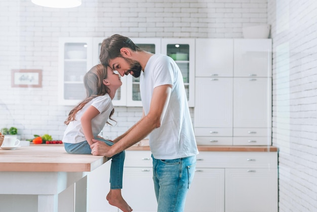 Padre y su hija con delantales mirándose en la cocina doméstica