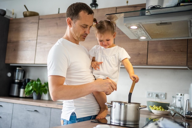 Padre con su hija en las manos cocinando sopa juntos en la cocina casera moderna