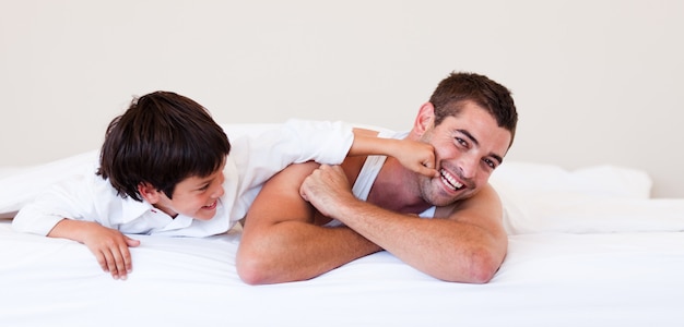 Padre y su hijo divirtiéndose en una cama.