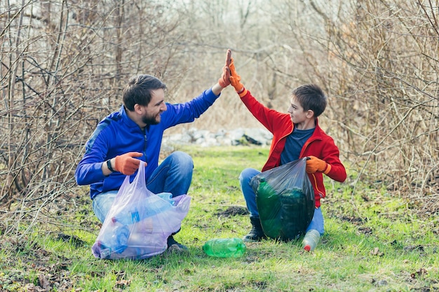 Un padre y su hijo limpian el parque de basura voluntarios limpian el bosque de botellas de plástico y pasan tiempo juntos regocijándose por el trabajo realizado y los beneficios para el medio ambiente