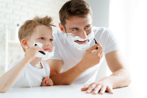 Padre y su pequeño hijo afeitándose juntos en el baño.