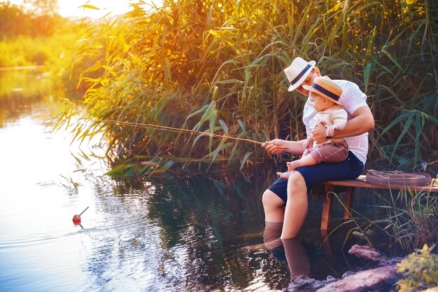 Padre con su pequeño hijo están pescando sentado en un muelle de madera junto al estanque.