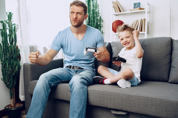 Padre y su pequeño hijo jugando videojuegos juntos en el sofá en casa