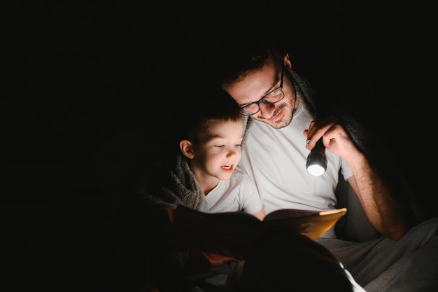 Padre y su pequeño hijo leyendo un cuento antes de dormir en casa