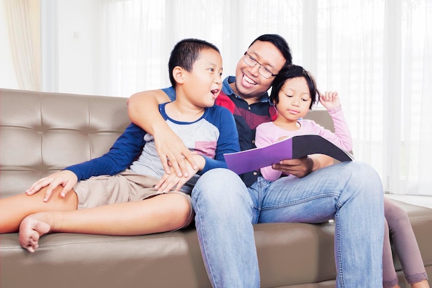 Padre y sus dos hijos leyendo un libro en casa