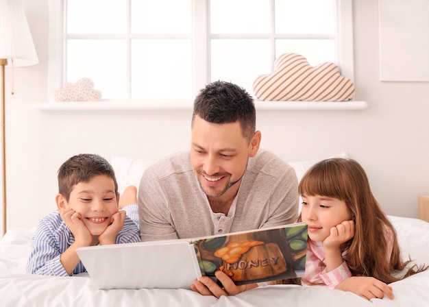 Padre y sus hijos pequeños leyendo un cuento antes de dormir en casa