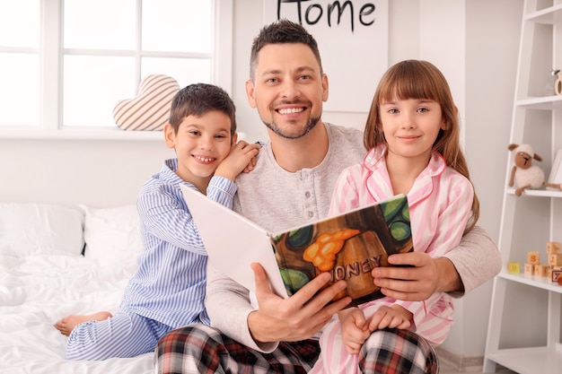 Padre y sus hijos pequeños leyendo un cuento antes de dormir en casa