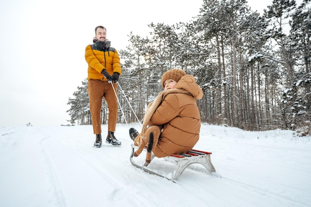 Padre tirando de un hijo pequeño en trineo en invierno