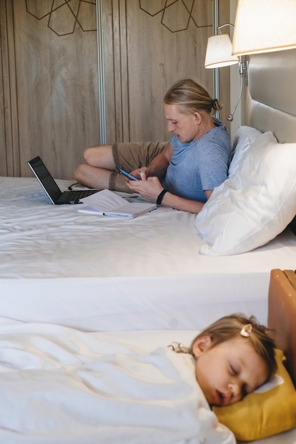 Padre trabajando mientras el niño se resbala en la cama en el hotel