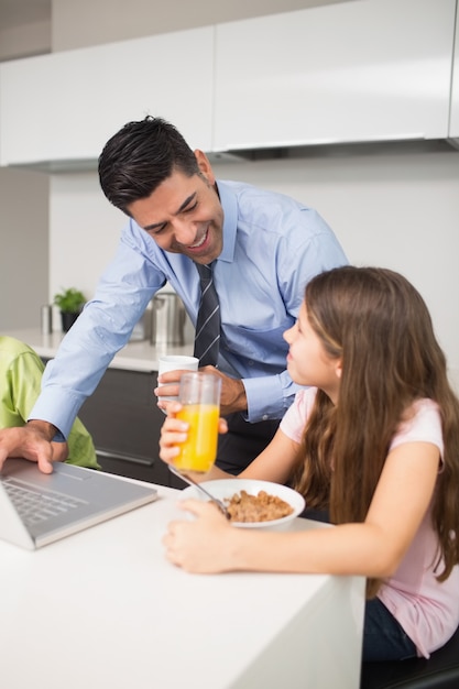 Padre usando laptop y niños desayunando en la cocina