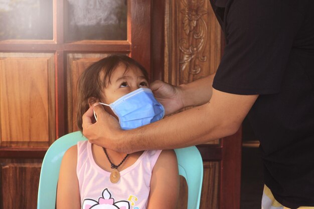 Foto padre vistiendo a su hija con una máscara facial en casa