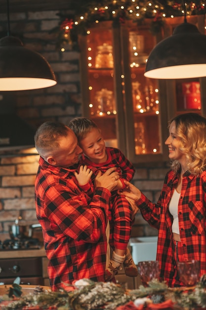 Foto los padres activos sonrientes con el hijo pequeño en pijama a cuadros rojos esperando a papá noel en el interior