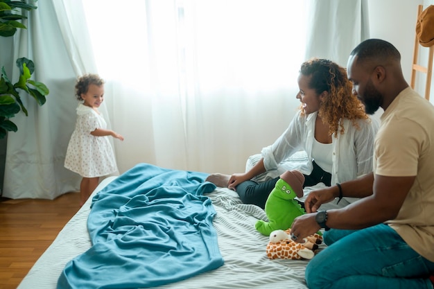 Padres afroamericanos felices con hijas pequeñas jugando en la cama en el dormitorio en casa