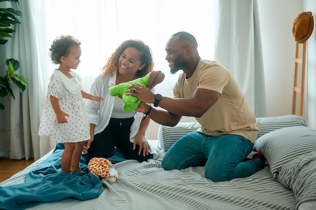 Padres afroamericanos felices con hijas pequeñas jugando en la cama en el dormitorio en casa