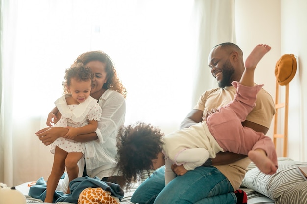 Padres afroamericanos felices con hijas pequeñas jugando en la cama en el dormitorio en casa