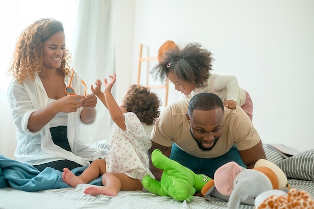 Padres afroamericanos felices con hijas pequeñas jugando en la cama en el dormitorio en casa