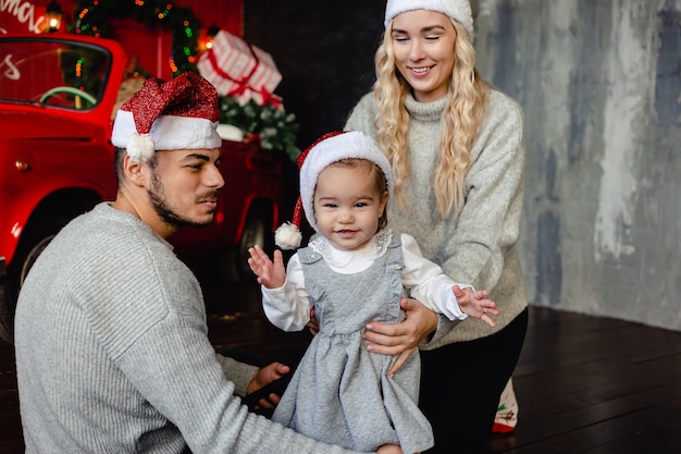 Padres alegres con hija en gorro de Papá Noel en casa con fondo de Navidad. Padre e hijo se divierten. ¡Feliz Navidad y Felices Fiestas!