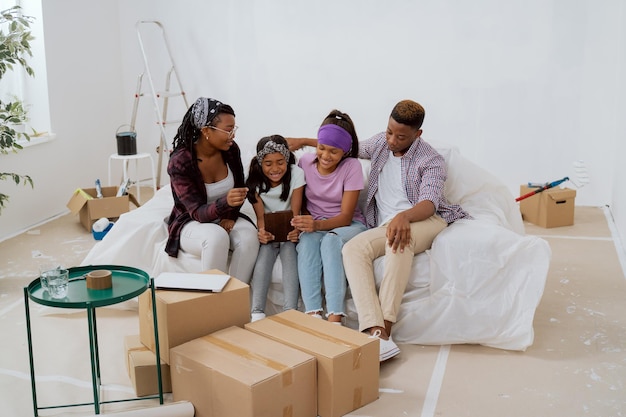 Los padres alegres y sus hijas están sentados en el apartamento durante la renovación