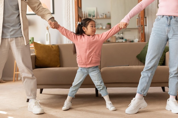 Padres asiáticos tirando de las manos de sus hijas en diferentes direcciones de pie en el interior