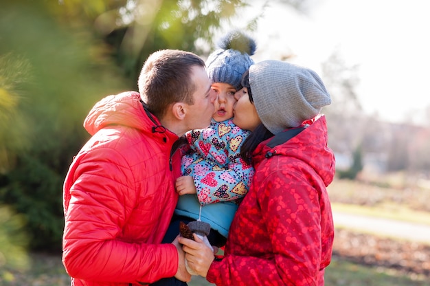 Los padres besan al niño en el parque de otoño