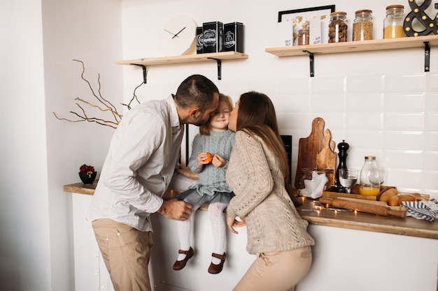Foto padres besando a su hija en la cocina en casa.