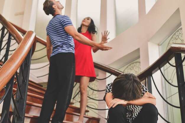 Foto los padres discuten mientras el hijo está sentado en la escalera en casa