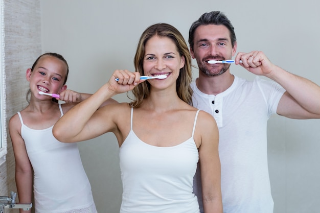 Foto padres e hija se cepillan los dientes en el baño