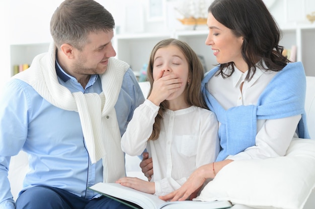 Padres e hija leyendo un libro grande en la habitación