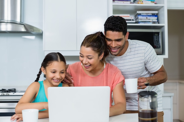 Padres e hija usando la computadora portátil en la cocina en casa