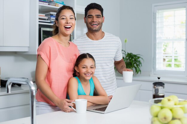 Padres e hija usando laptop mientras tomando un café en la cocina en casa