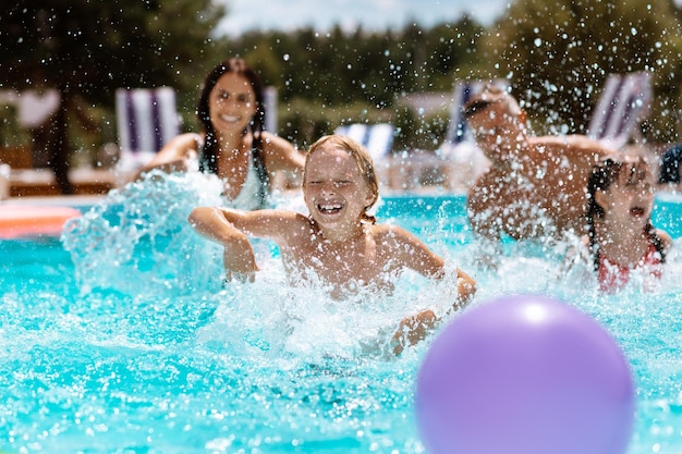 Padres e hijos riendo mientras juegan a la pelota en la piscina