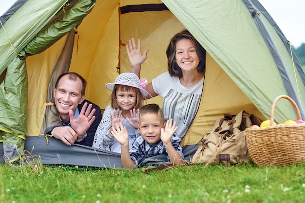 Los padres de familia y dos niños en la carpa del campamento. Feliz madre, padre, hijo e hija de vacaciones de verano.