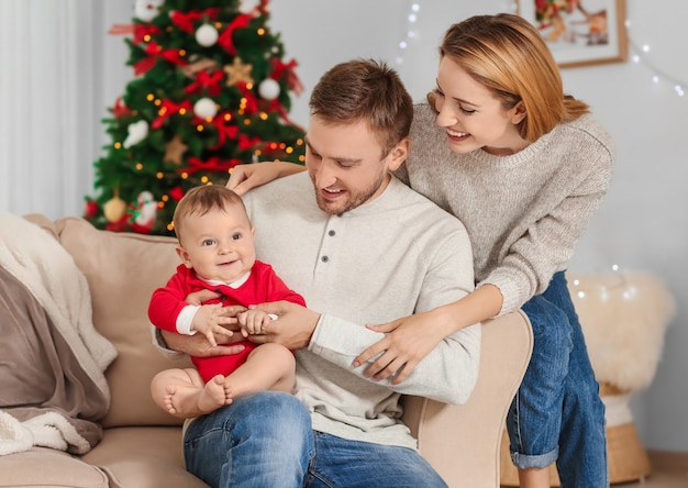 Padres felices con bebé en habitación decorada para Navidad