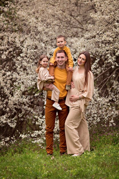 Los padres felices embarazadas mamá y papá, hija e hijo en el fondo de los árboles en flor.