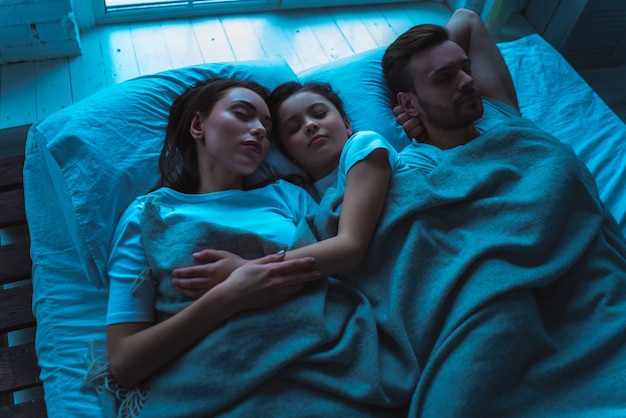 Los padres y una hija acostados en la cama. tarde noche