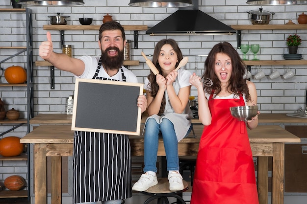 Padres con hija cocinando en casa niña ayuda a madre y padre Tradiciones familiares familia preparando comida en la cocina juntos mamá papá y niño sostienen pizarra pasan tiempo libre juntos copia espacio