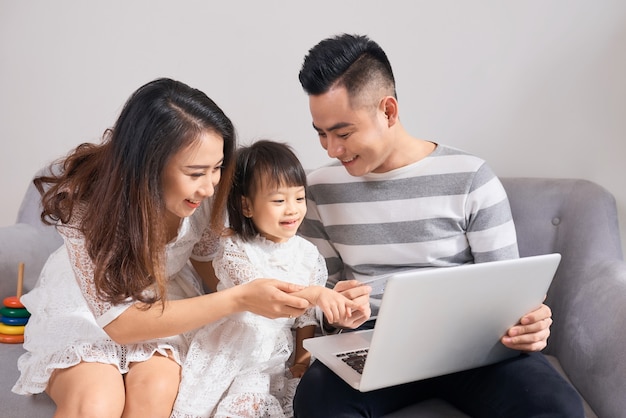 Los padres y la hija jugando junto con un portátil en un sofá