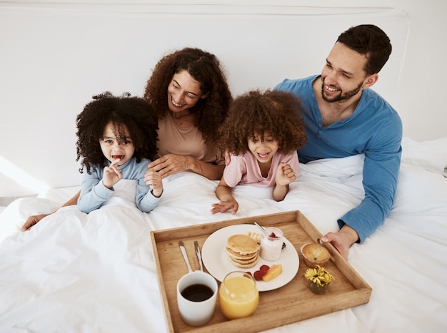Padres, hijos y desayuno en la cama por la mañana o emocionados por el vínculo amoroso o el cuidado durante las vacaciones. Madre, papá y niños en la comida del dormitorio y sonríen juntos para comer nutrición y un hogar familiar feliz.