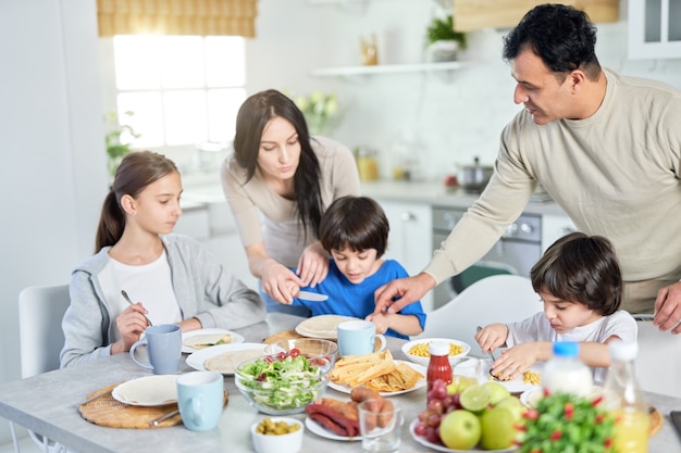 Padres hispanos amorosos que sirven a sus hijos pequeños mientras almuerzan juntos en casa. Infancia, paternidad, concepto de cocina latina