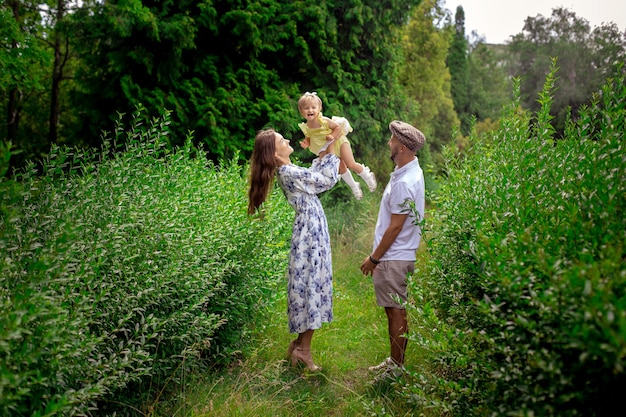 Padres jóvenes alegres jugando con su pequeña niña en el jardín verde. Familia feliz divirtiéndose en el parque