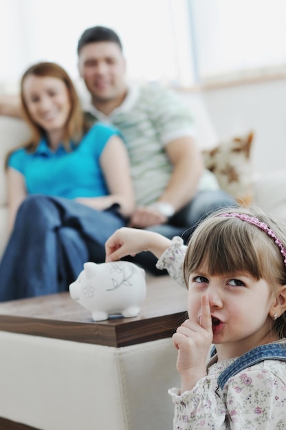 los padres jóvenes en casa con un niño hermoso hacen ahorros y ponen monedas en una alcancía