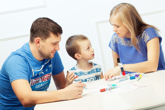 Padres jóvenes dibujando en la mesa con su hijo