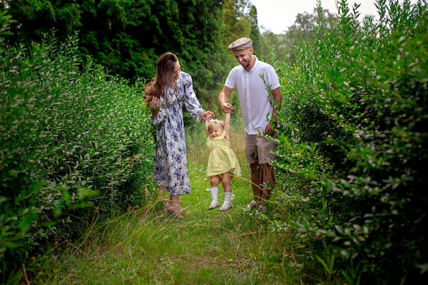 Padres jóvenes felices jugando con su pequeña niña en el jardín verde. Familia alegre divirtiéndose en el parque