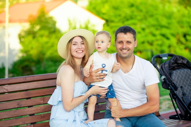 Los padres jóvenes felices mamá y papá con su hijo caminan en el parque en el verano en un banco y se divierten y sonríen