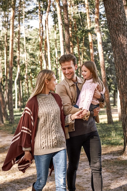 Padres jóvenes con hija pequeña en bosque de otoño