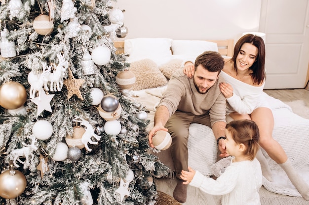 Padres jóvenes con una hija pequeña cerca del árbol de Navidad