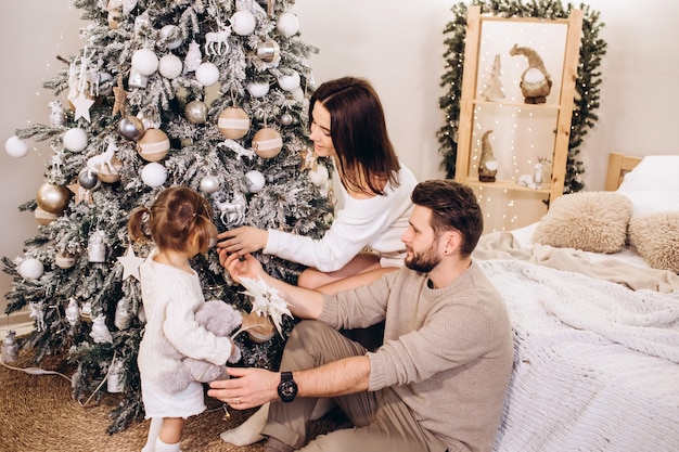 Padres jóvenes con una hija pequeña cerca del árbol de Navidad