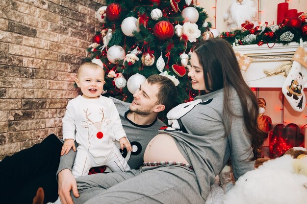 Padres jóvenes con hijo cerca del árbol de Navidad